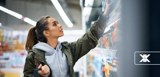 Mulher escolhendo produtos em prateleira de supermercado iluminado.