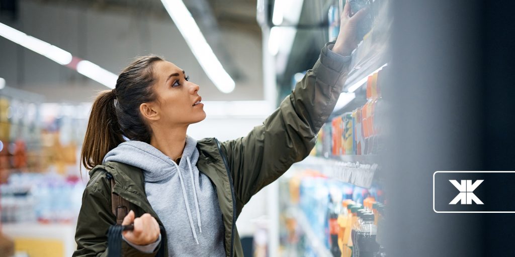 Woman choosing products on illuminated supermarket shelf.